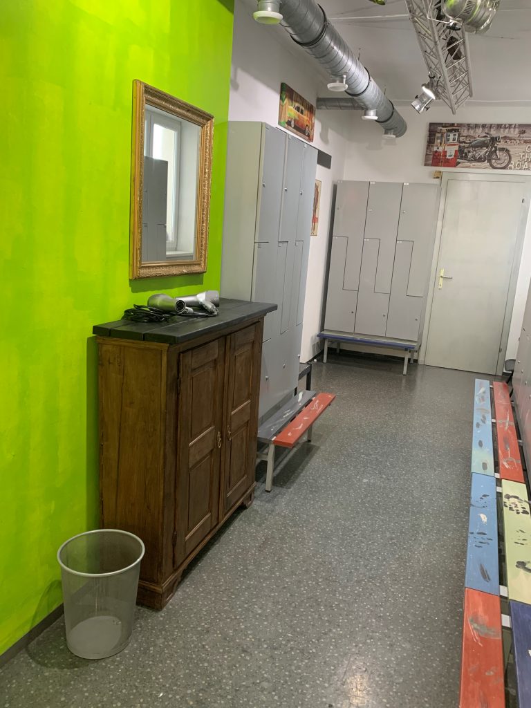 Herrenumkleide, grüne Wand mit Fönplatz altes braunes Kastl, Spints mit bunten Sitzbankerln